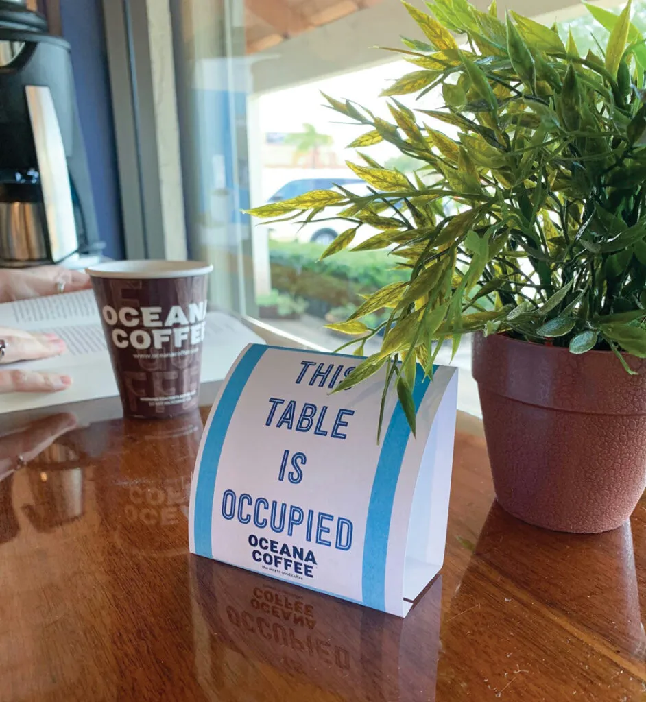 AT OCEANA COFFEE’S two locations, table place cards reserve a customer’s seat for the duration of their stay. Once they’ve left, the sign stays until staff have wiped down and sanitized the table and chair.
