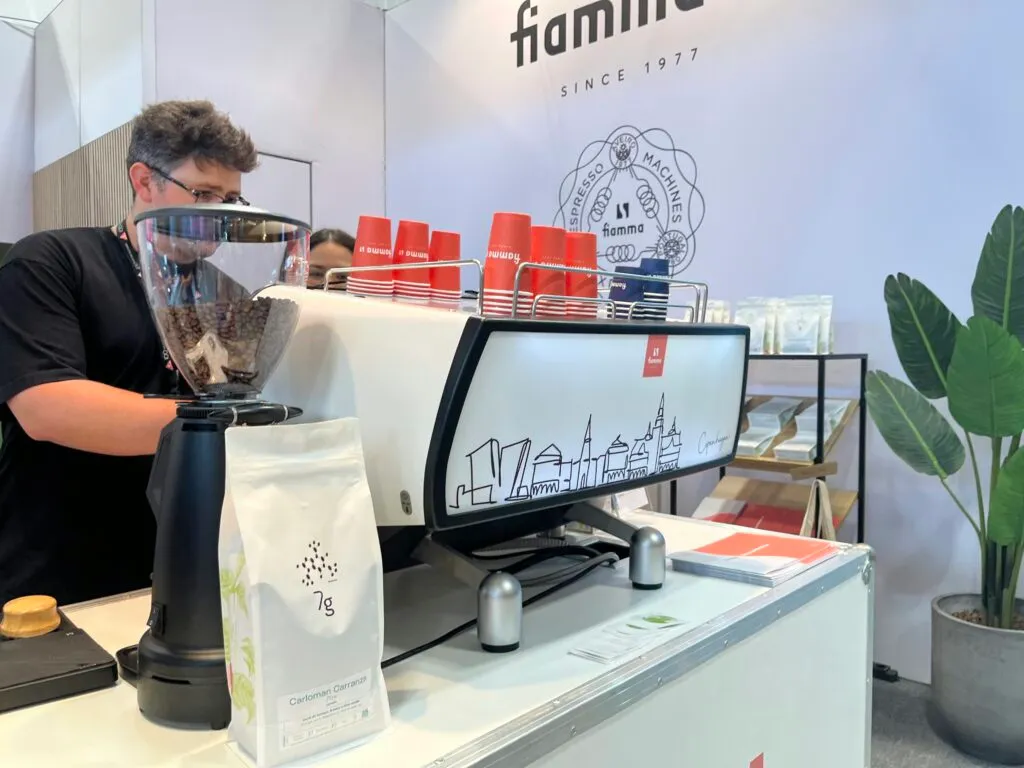 A 7G barista behind a Fiamma espresso machine with a line drawing of the Copenhagen skyline.
