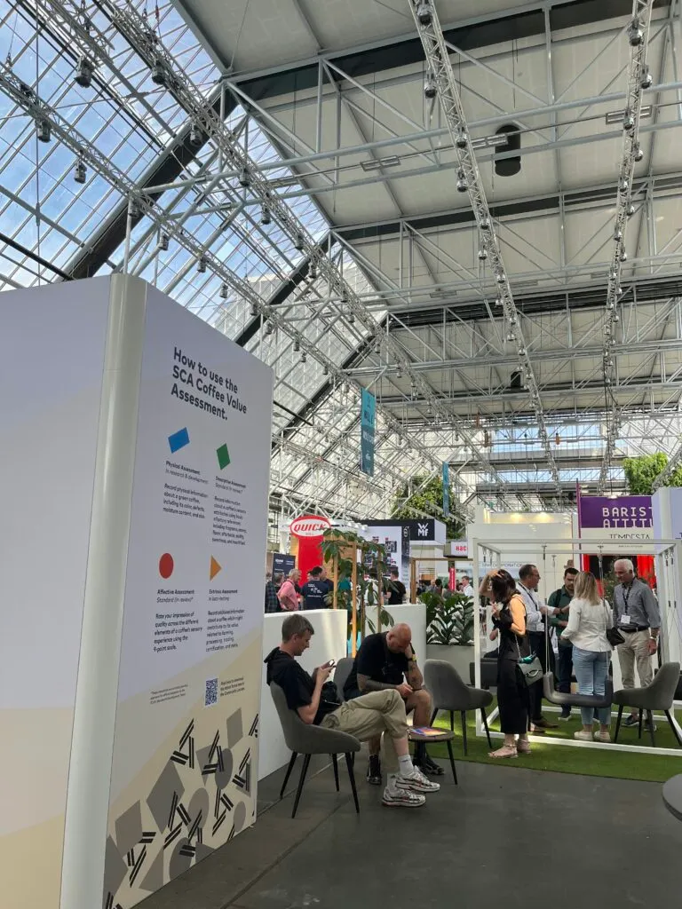 Visitors relaxing in the SCA community space next to a poster explaining the Coffee Value Assessment.